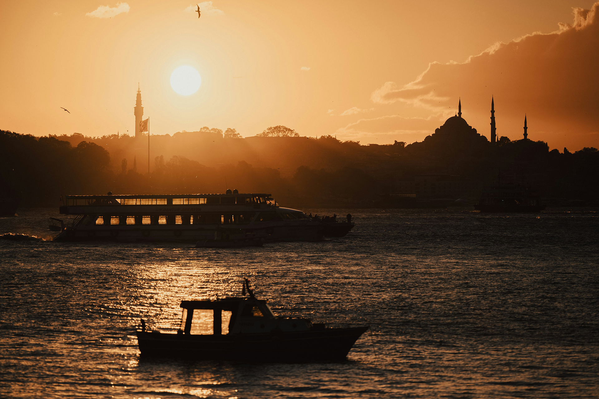 Istanbul skyline at sunset over the Bosphorus, with mosque silhouette and boats on the water